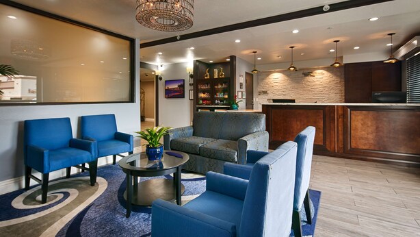 A modern living room with blue sofas, a coffee table, and a TV. There is a kitchen area with a bar and a stone wall. - Best Western Plus Diamond Valley Inn (Hemet)