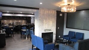 A modern lounge area with blue seating, a fireplace, and a kitchen in the background. - Best Western Plus Diamond Valley Inn (Hemet)