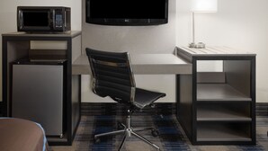 Une chambre d’hôtel équipée d’un bureau, d’une télévision à écran plat, d’un four à micro-ondes, d’une chaise, d’une lampe et d’un mini-réfrigérateur.