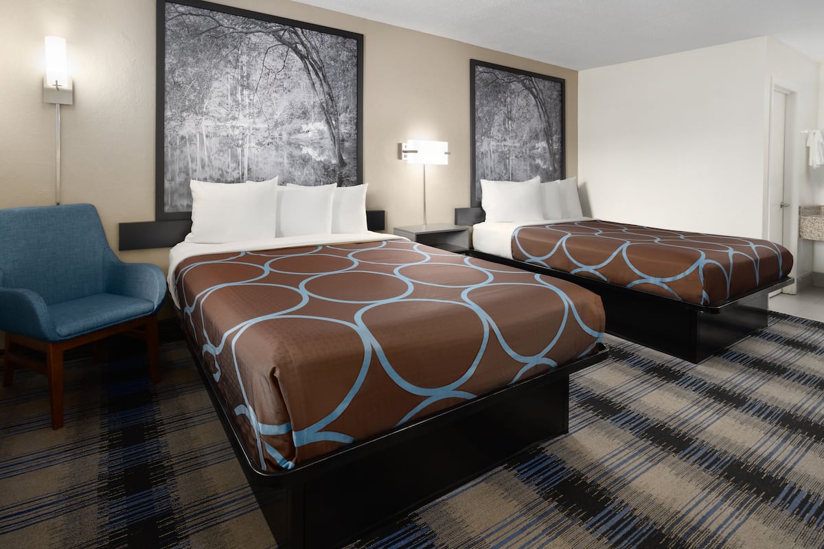 Quarto de hotel com duas camas, uma cadeira azul e uma pintura grande na parede.