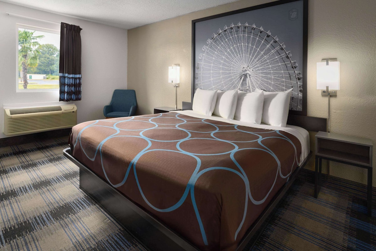 Quarto de hotel com uma cama grande, uma poltrona, uma luminária fixada na parede e uma grande decoração na parede.