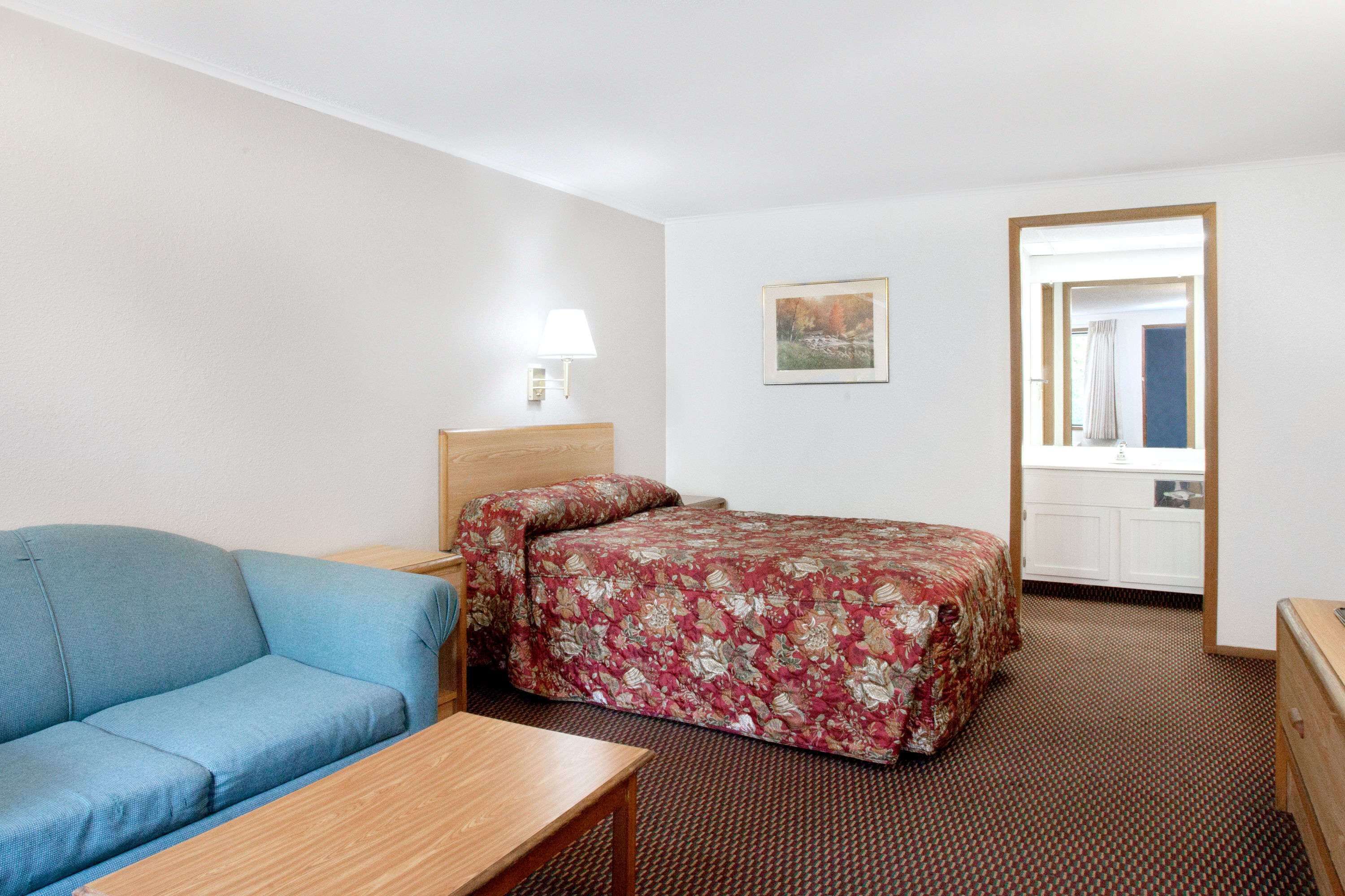Una habitación de hotel con cama, sofá, mesita de noche, lámpara y un cuadro en la pared.