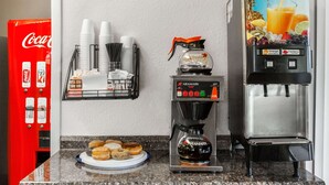 A coffee station with a coffee maker, a juice dispenser, and a plate of pastries.