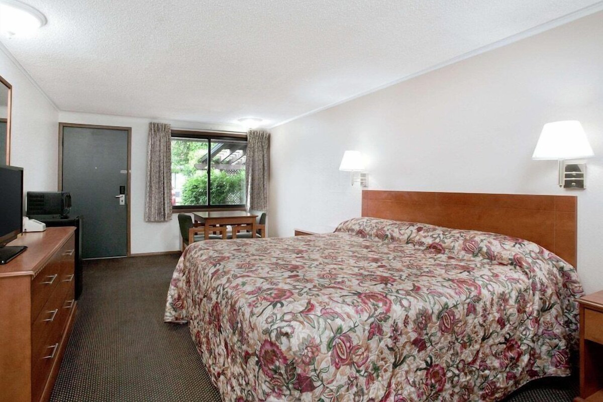 Een hotelkamer met een bed, een bureau met stoel, een televisie en een raam met gordijnen.