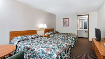 A hotel room with two beds, a desk, a chair, a TV, and a bathroom visible through an open door.