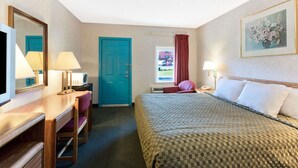 Habitación de hotel con cama, escritorio con silla, televisión, puerta y ventana con vista al exterior.