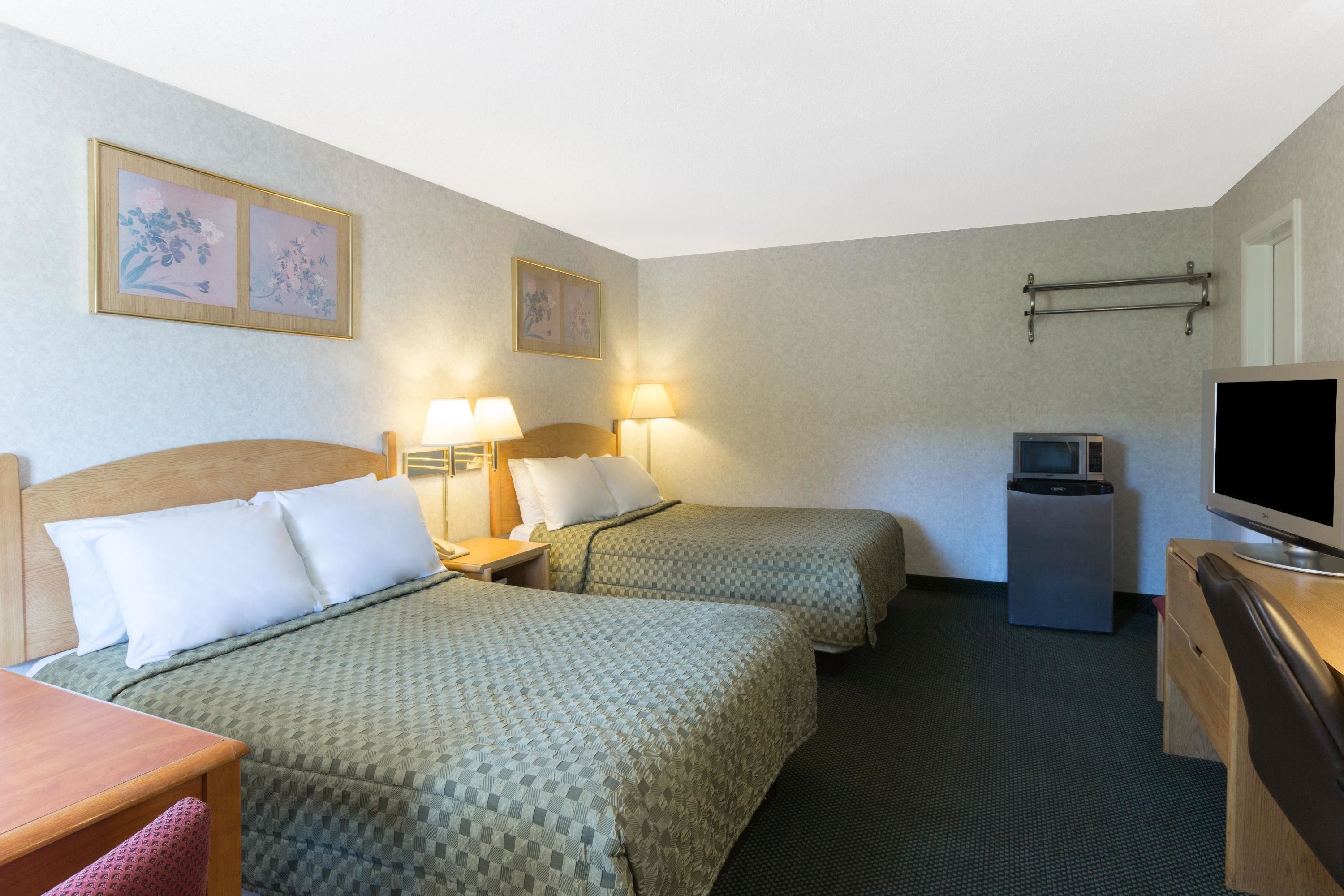 Een hotelkamer met twee bedden, een bureau, een televisie en een kleine koelkast.