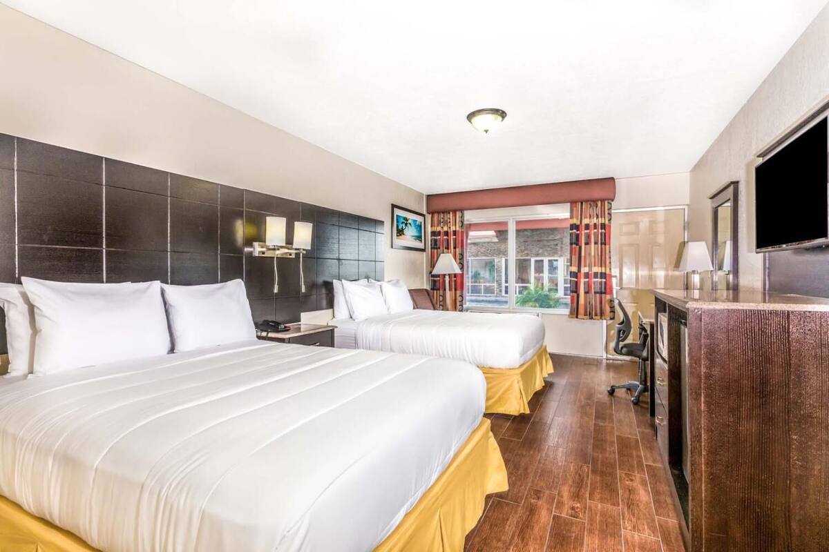 A hotel room with two beds, a desk, a TV, and a window with curtains.