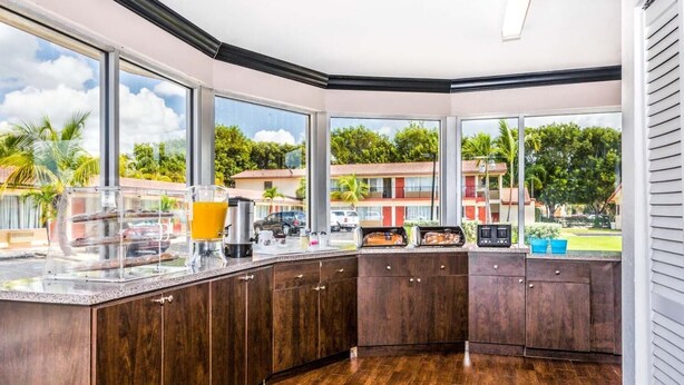 A modern kitchen with dark wood cabinets, a granite countertop, and large windows offering a view of the neighborhood. - Econo Lodge Inn & Suites Florida City (Florida City)