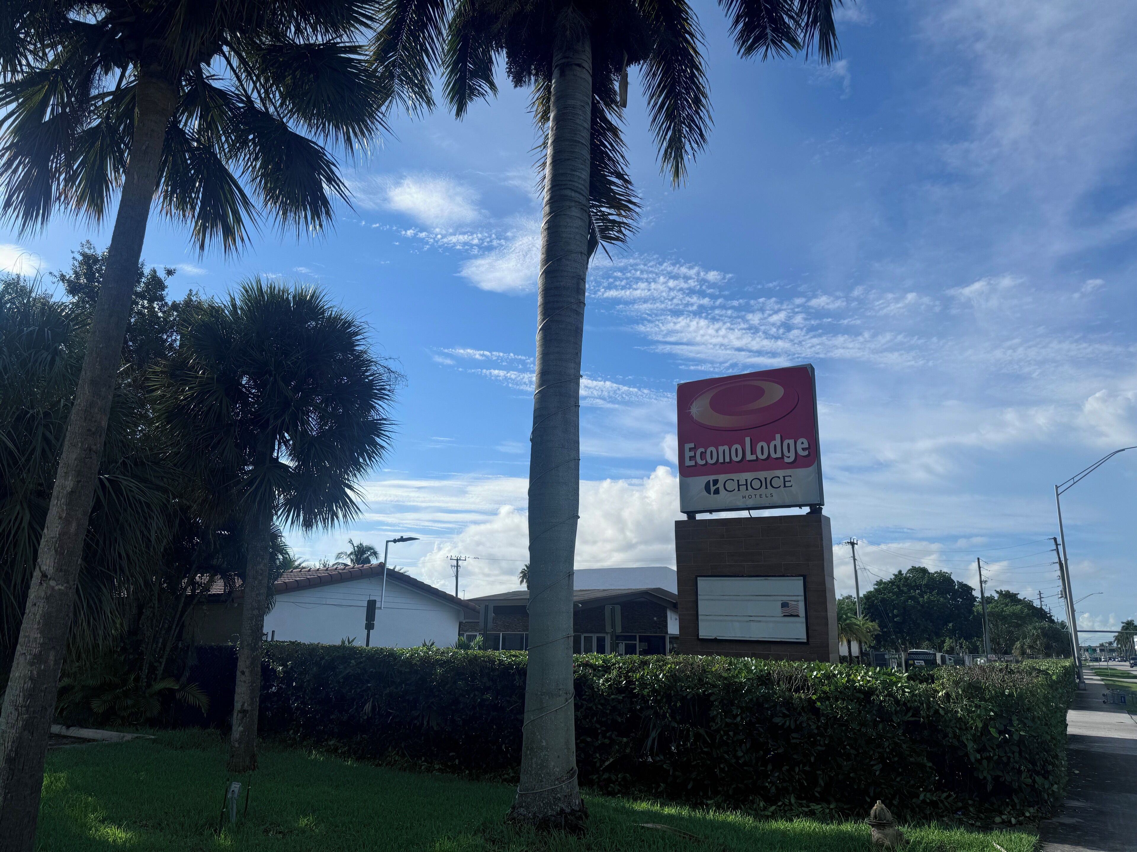 Een hotelschild voor EconoLodge met het logo van Choice Hotels, omgeven door palmbomen en een heldere lucht.