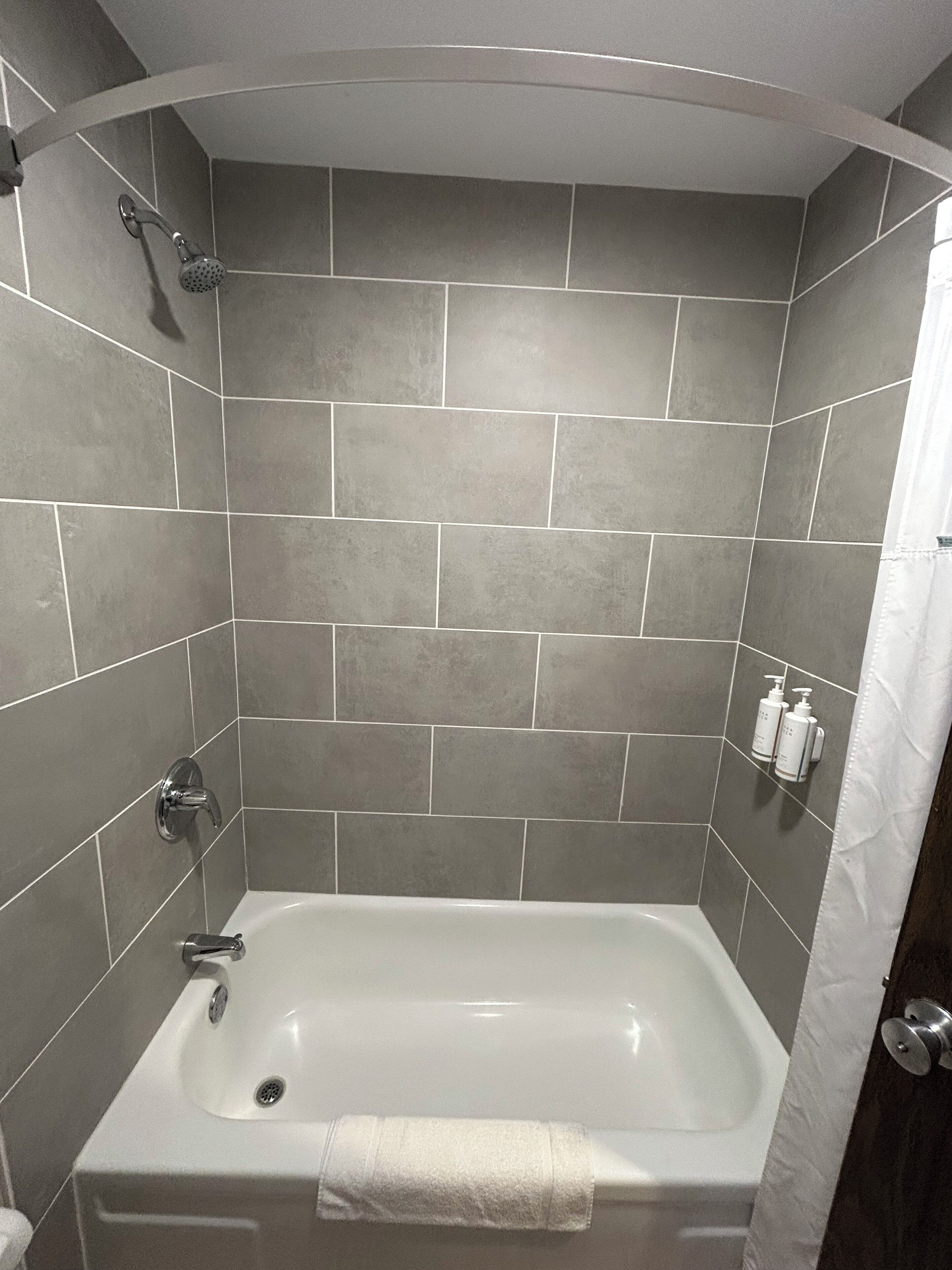 A modern bathroom with a freestanding bathtub, grey tiled walls, and a showerhead.