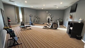 Sala de ginástica de hotel com equipamentos de exercício, televisão e uma janela grande.