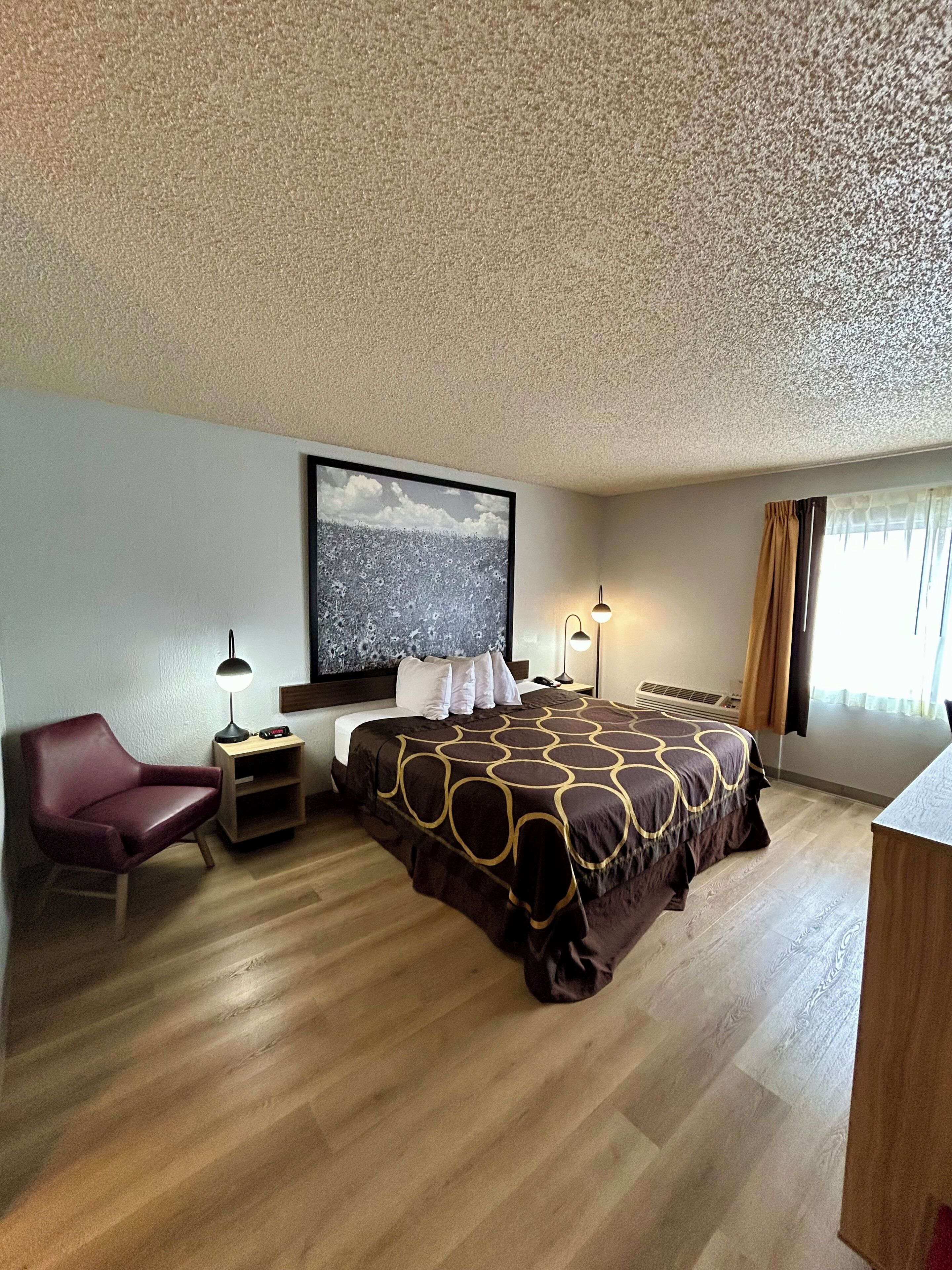 A hotel room with a large bed, a chair, a desk, and a wall-mounted TV.
