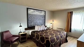 Ein Hotelzimmer mit einem großen Bett, einem Sessel, einem Schreibtisch und einem an der Wand befestigten Fernseher.
