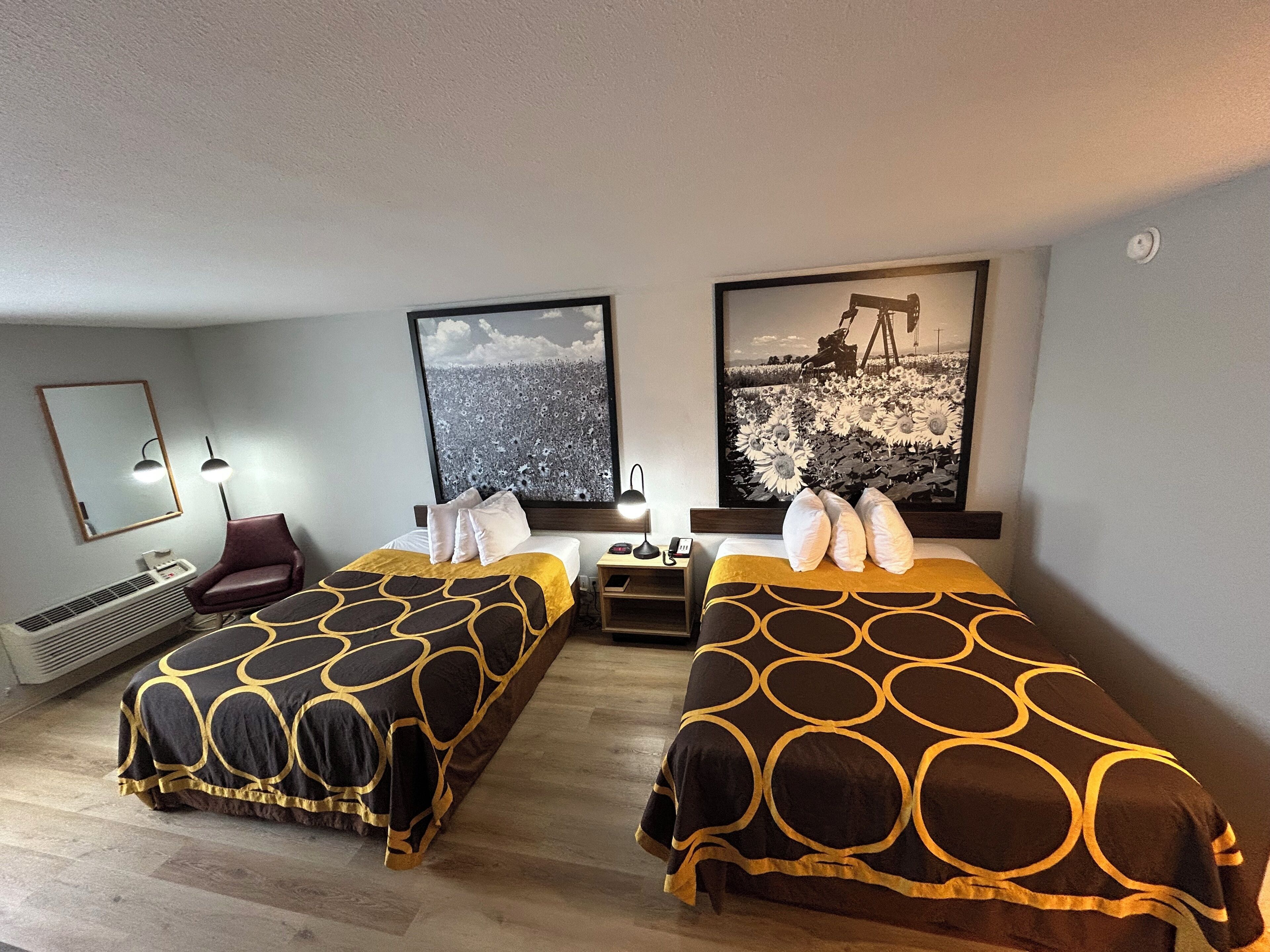 Ett hotellrum med två sängar, ett skrivbord, en stol och två stora tavlor som hänger på väggen.