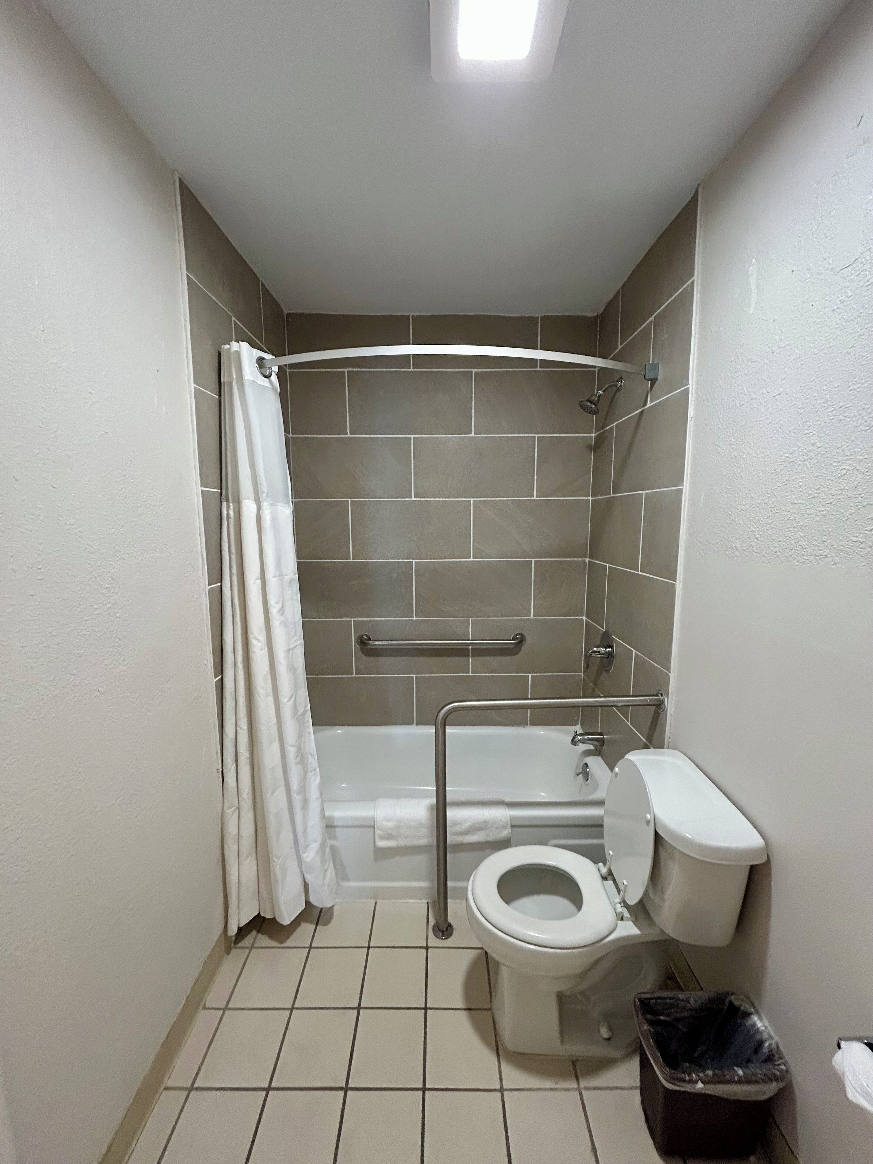 A small, clean bathroom with a toilet, shower, and grab bar.