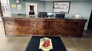 Bancada de recepção com relógio, pôster emoldurado e tapete preto com o logotipo "Super 8".