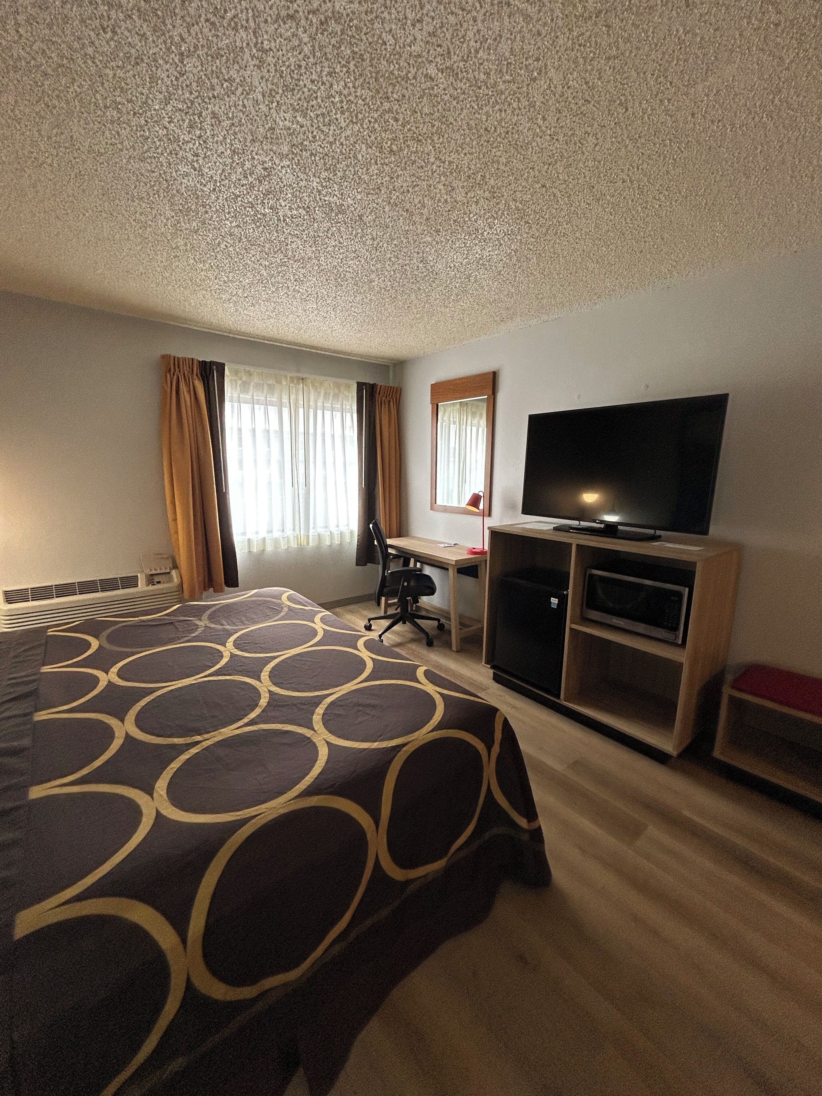 A hotel room with a large bed, a desk with a chair, a television, and a microwave.