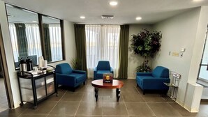 Ampla sala de estar com uma grande janela, dois sofás azuis, uma mesa de centro e um carrinho com comodidades.