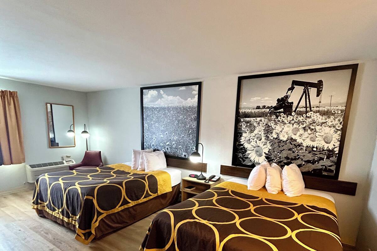 Une chambre d’hôtel avec deux lits, une grande fenêtre et un tableau représentant un champ de tournesols.