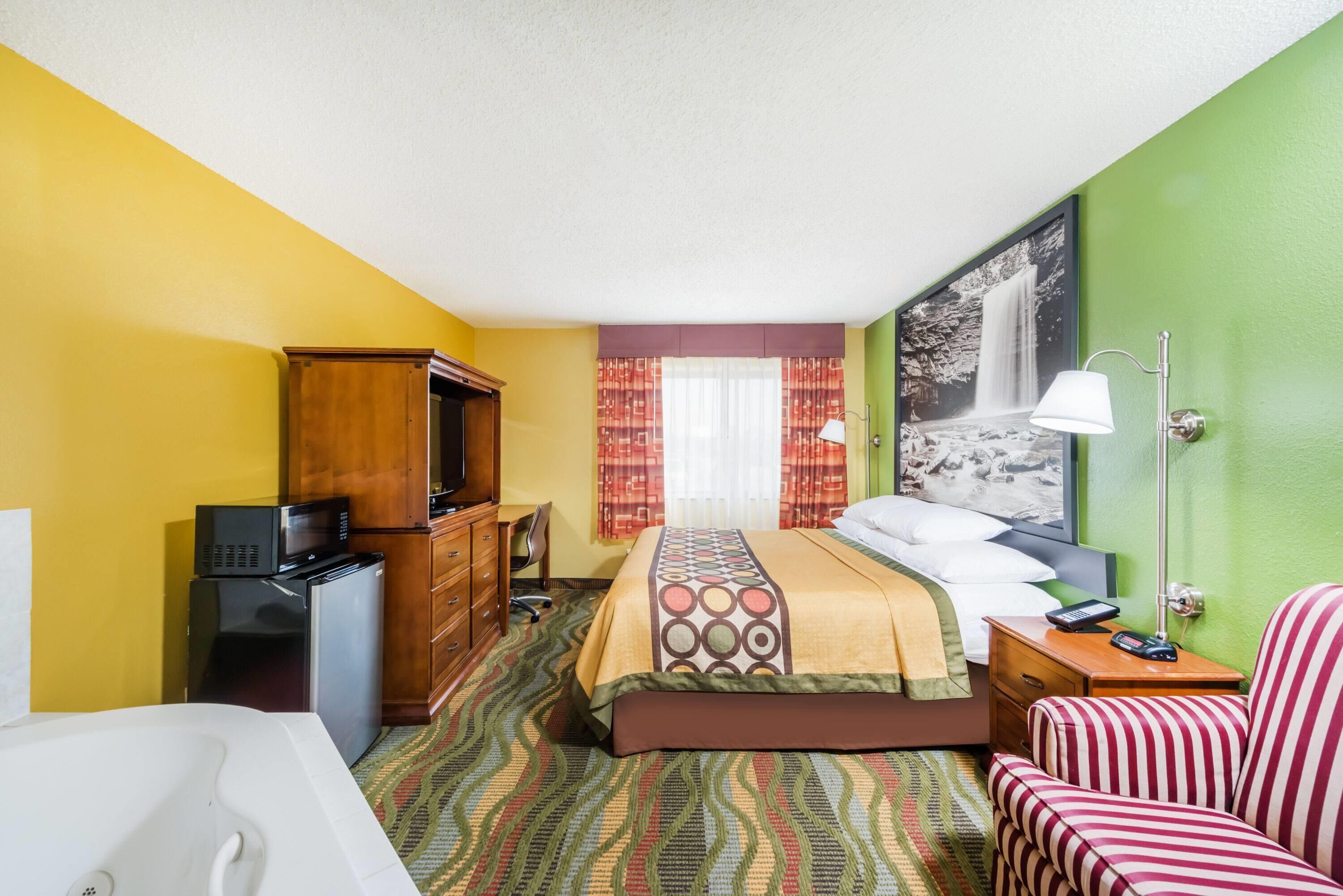 Camera d'albergo con un letto, una scrivania, una sedia, una televisione, un frigorifero e un bagno con una vasca.