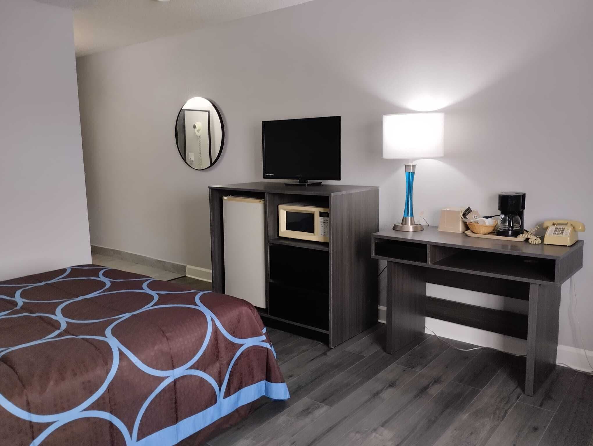 Una habitación de hotel con cama, escritorio con lámpara, televisión, microondas y teléfono.