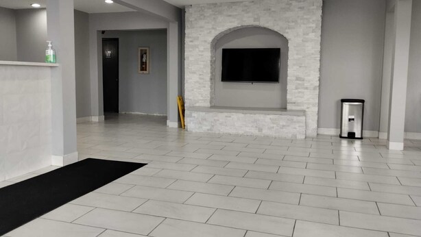 A spacious room with a tiled floor, a stone accent wall, a mounted TV, and a trash bin.