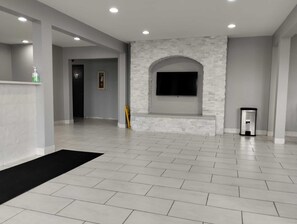 Ein geräumiges Zimmer mit Fliesenboden, einer Wand aus Stein und einem wandmontierten Fernseher. Ein Mülleimer ist ebenfalls vorhanden.