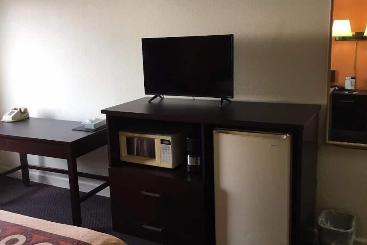 Habitación de hotel compacta con escritorio, refrigerador pequeño, microondas, teléfono y espejo.
