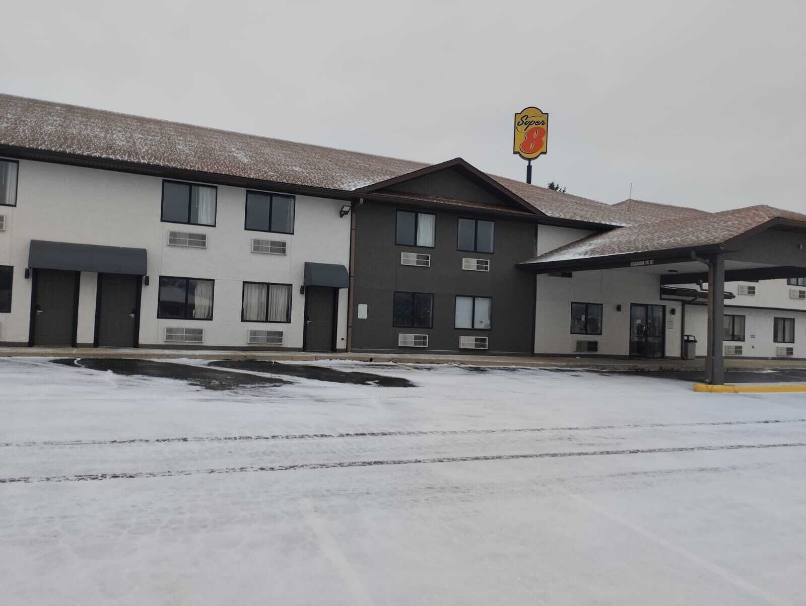 A motel with a Super 8 sign, multiple rooms, and a covered parking area.