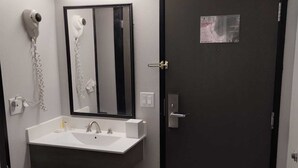 A bathroom with a white sink, a mirror, a hairdryer, and a door with an emergency exit sign.