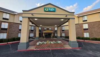Entrada do hotel Quality Inn, com galeria coberta, fachada de tijolos e placa sobre a entrada.