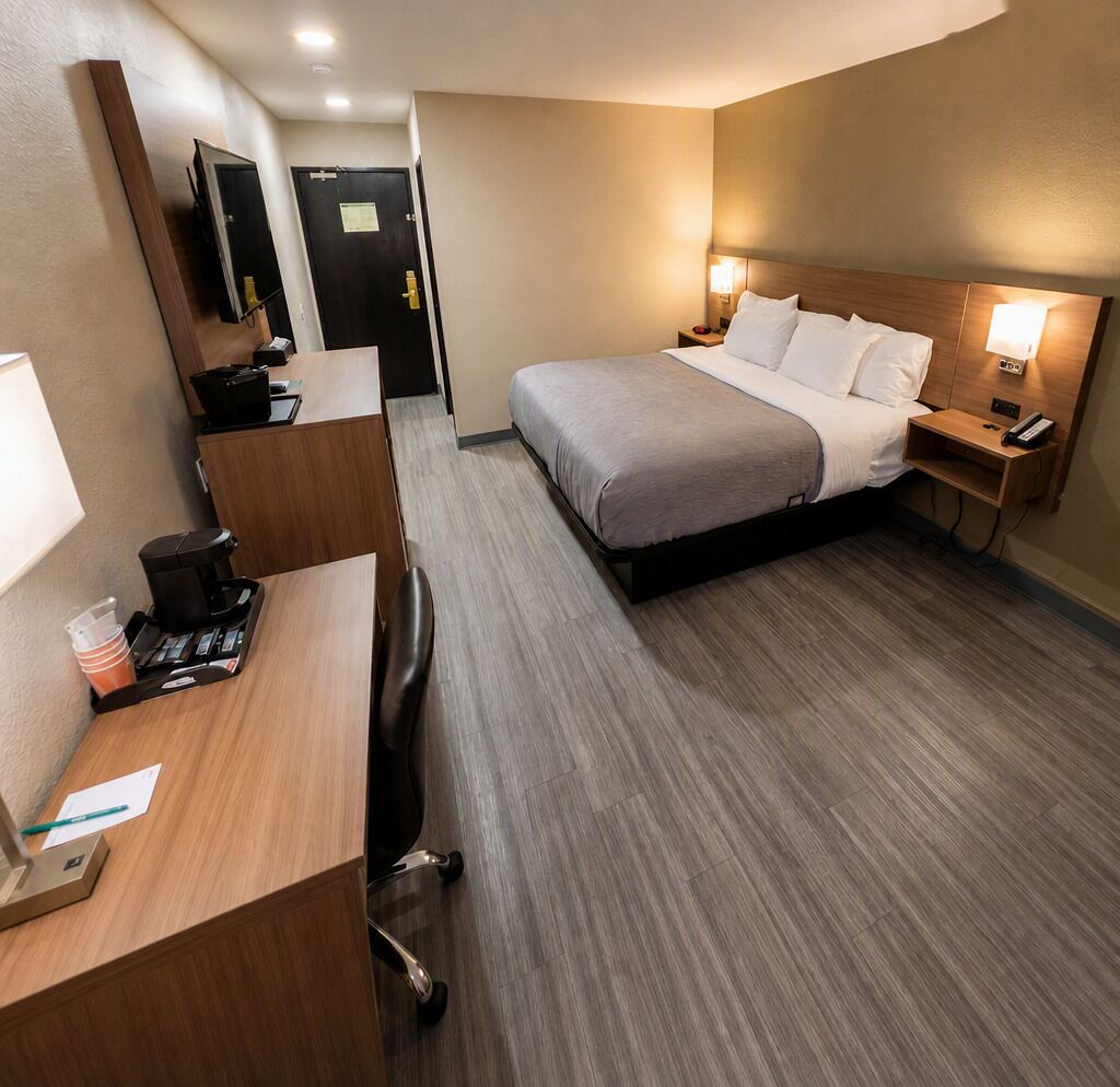 A hotel room with a bed, bedside tables, a desk, a chair, a coffee machine, and a mirror.