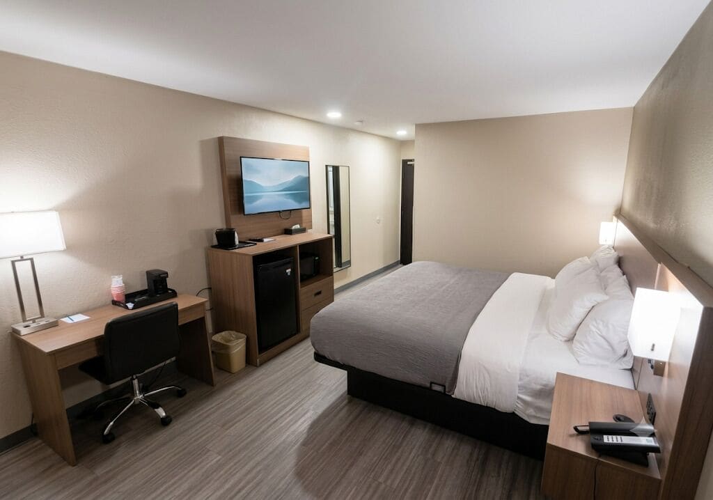Een hotelkamer met een bed, bureau, stoel, televisie en een klein kastje.