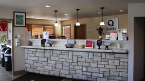 Zona de recepción de un hotel con mostrador de piedra, múltiples terminales de pago y un cartel que indica 'Quality by Choi'.
