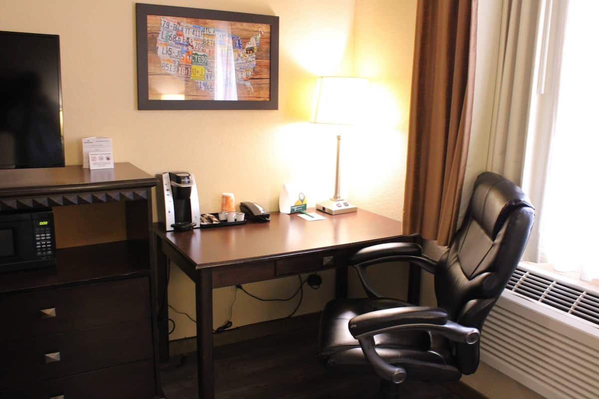 A hotel room with a desk, a black office chair, a lamp, a microwave, and a framed map on the wall.