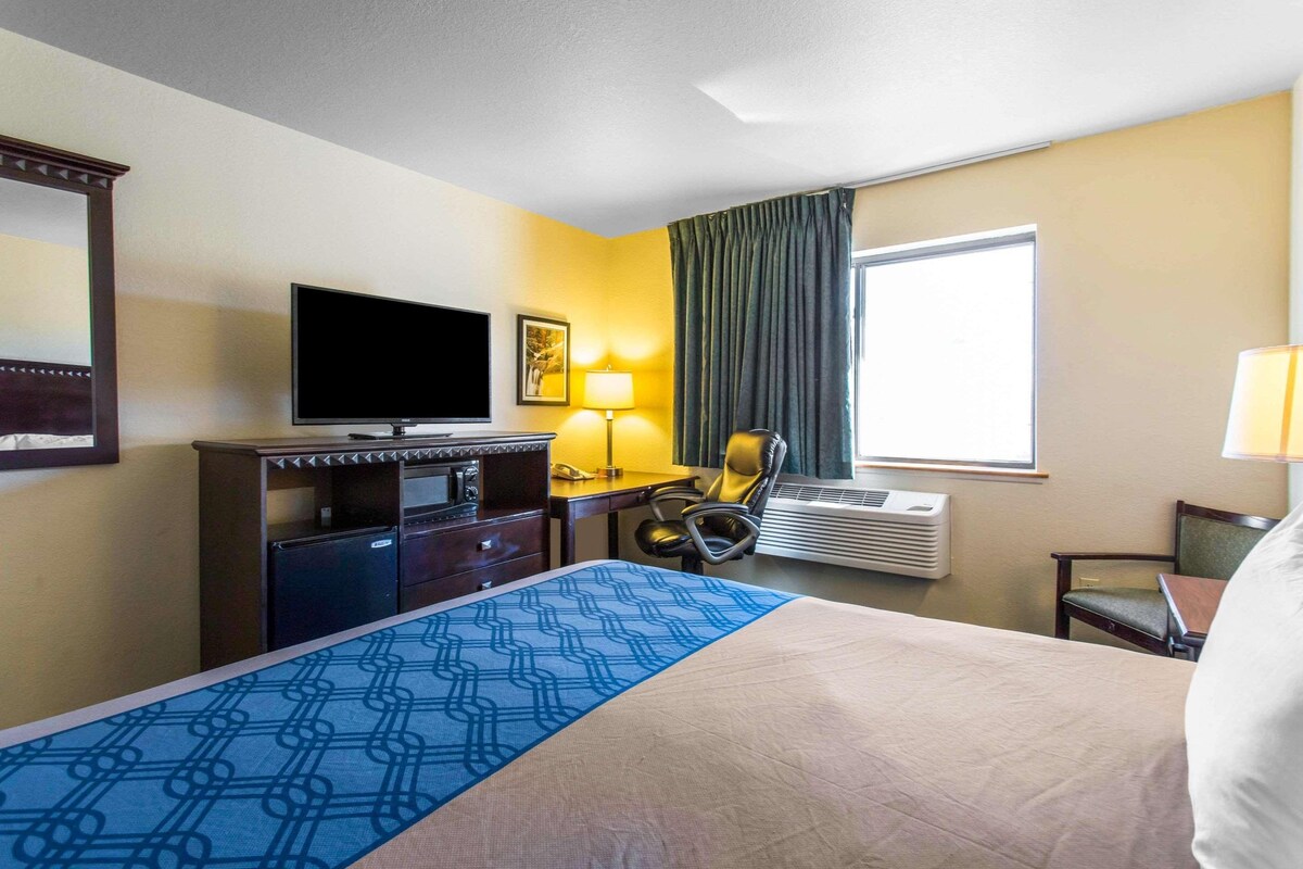 Habitación de hotel con cama, escritorio con silla, televisor, lámpara y equipo de aire acondicionado.