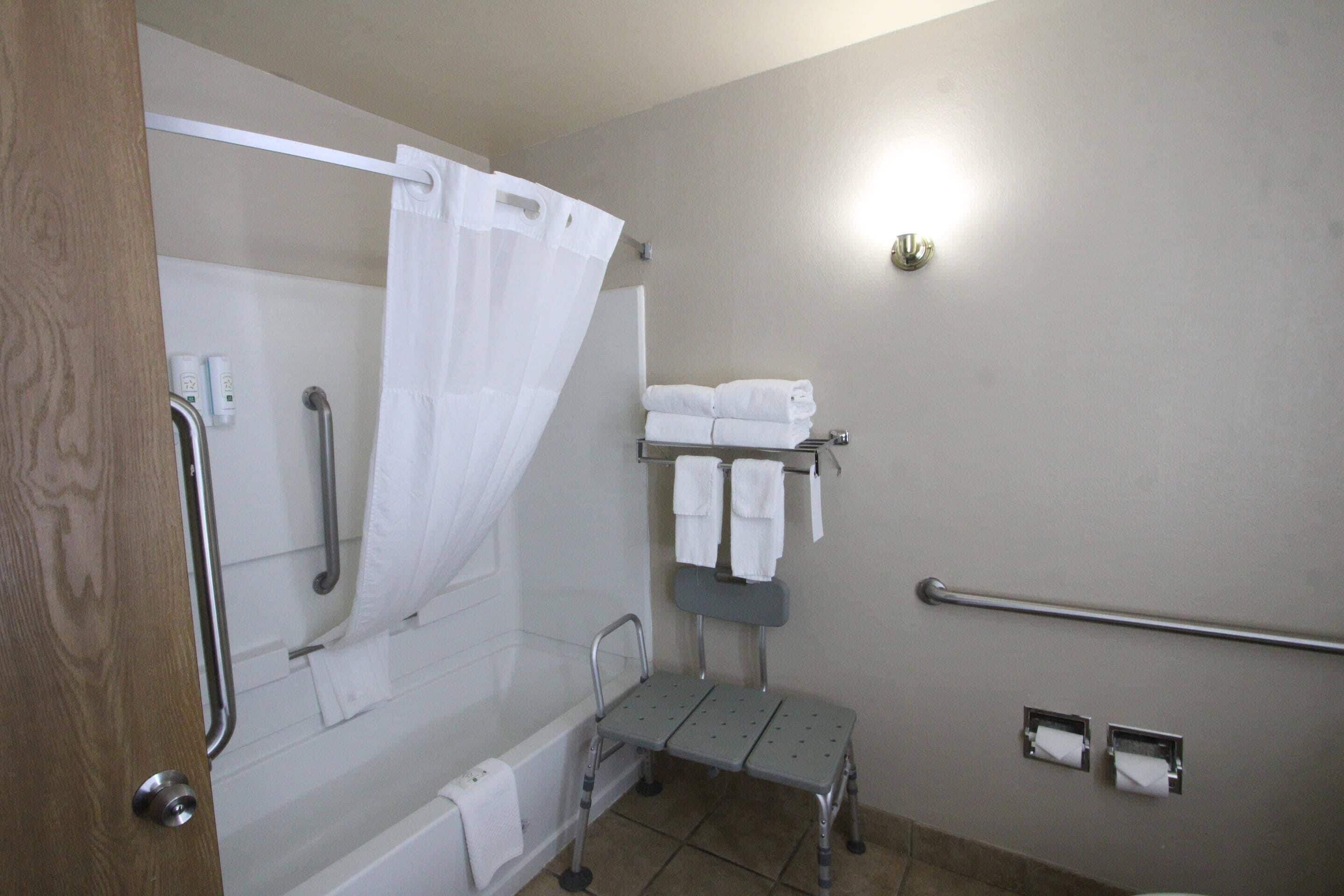 Ein Badezimmer mit Dusche, Haltegriffen, einer Sitzbank und einem Handtuchhalter.