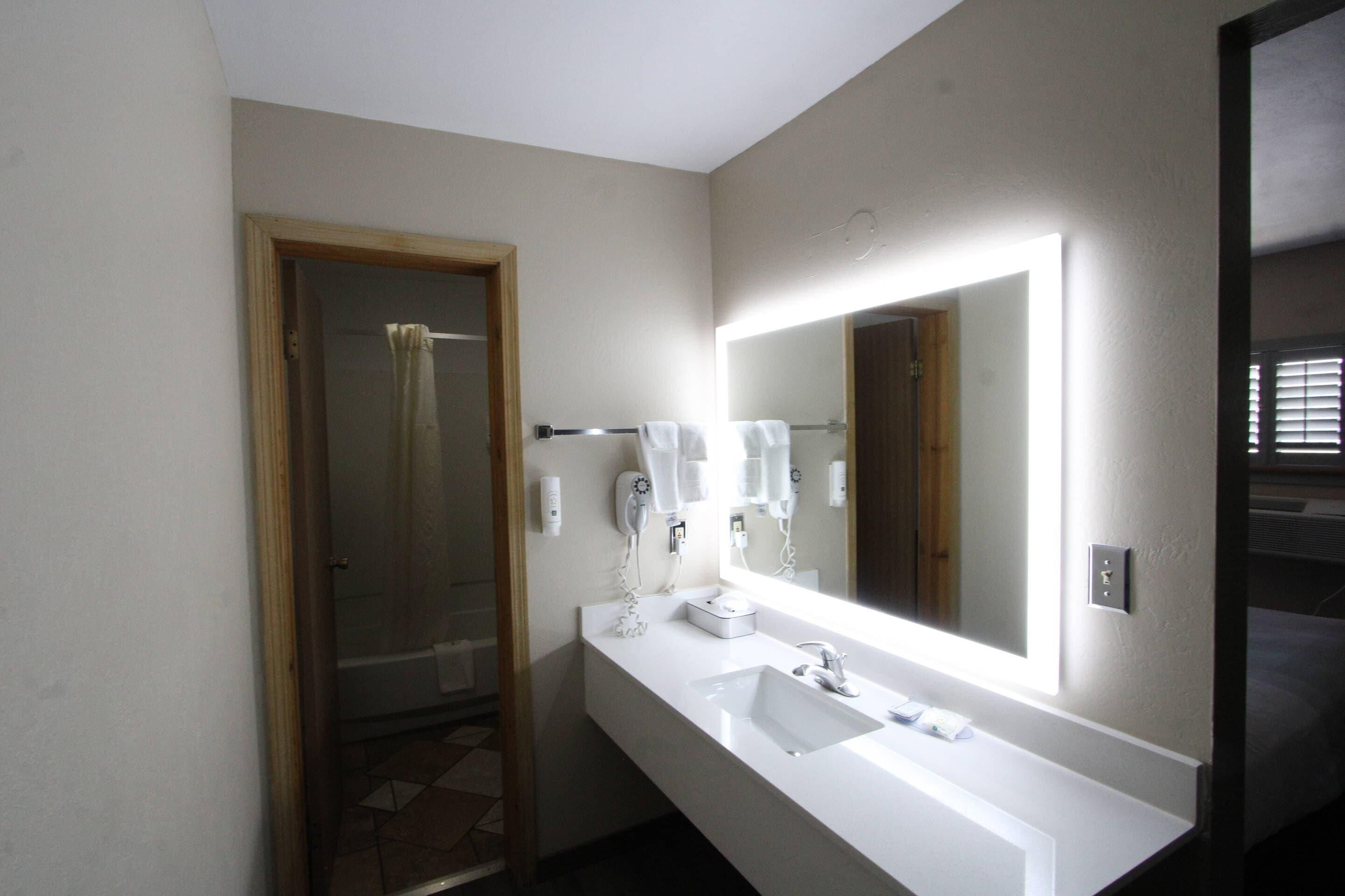 Une salle de bain avec un grand miroir, un lavabo blanc et un porte-serviettes.
