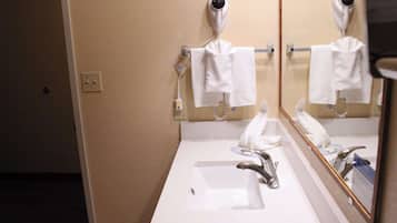A hotel bathroom with a white sink, a mirror, and two hair dryers mounted on the wall.