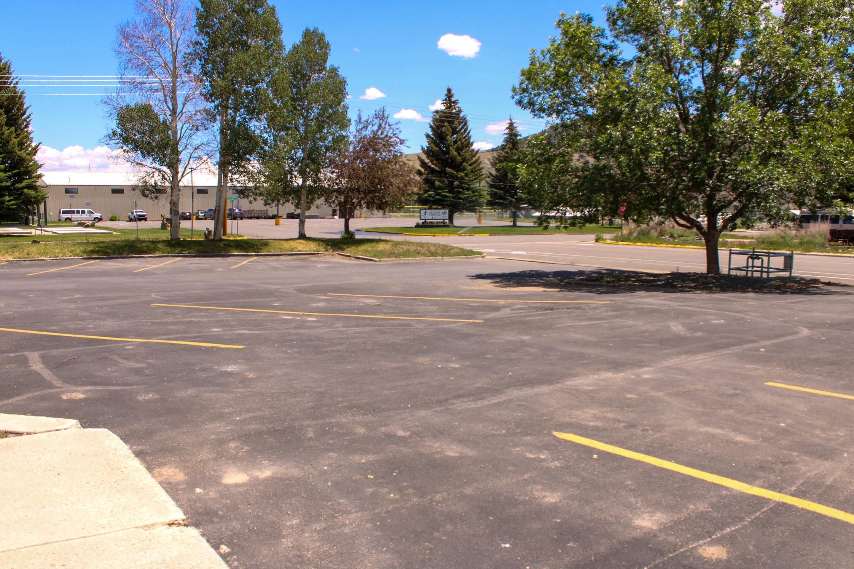 Un parking avec des places délimitées, un banc et des arbres.
