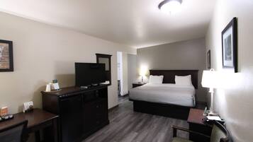 Habitación de hotel con cama, escritorio con televisor, silla y mesita de noche con lámpara.