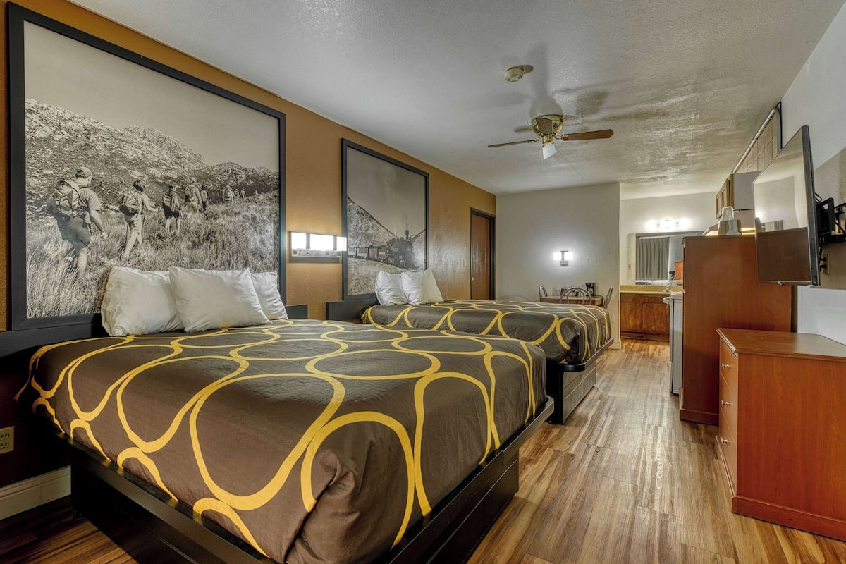 Une chambre d’hôtel avec deux lits, un ventilateur de plafond, un grand tableau encadré et une commode en bois.