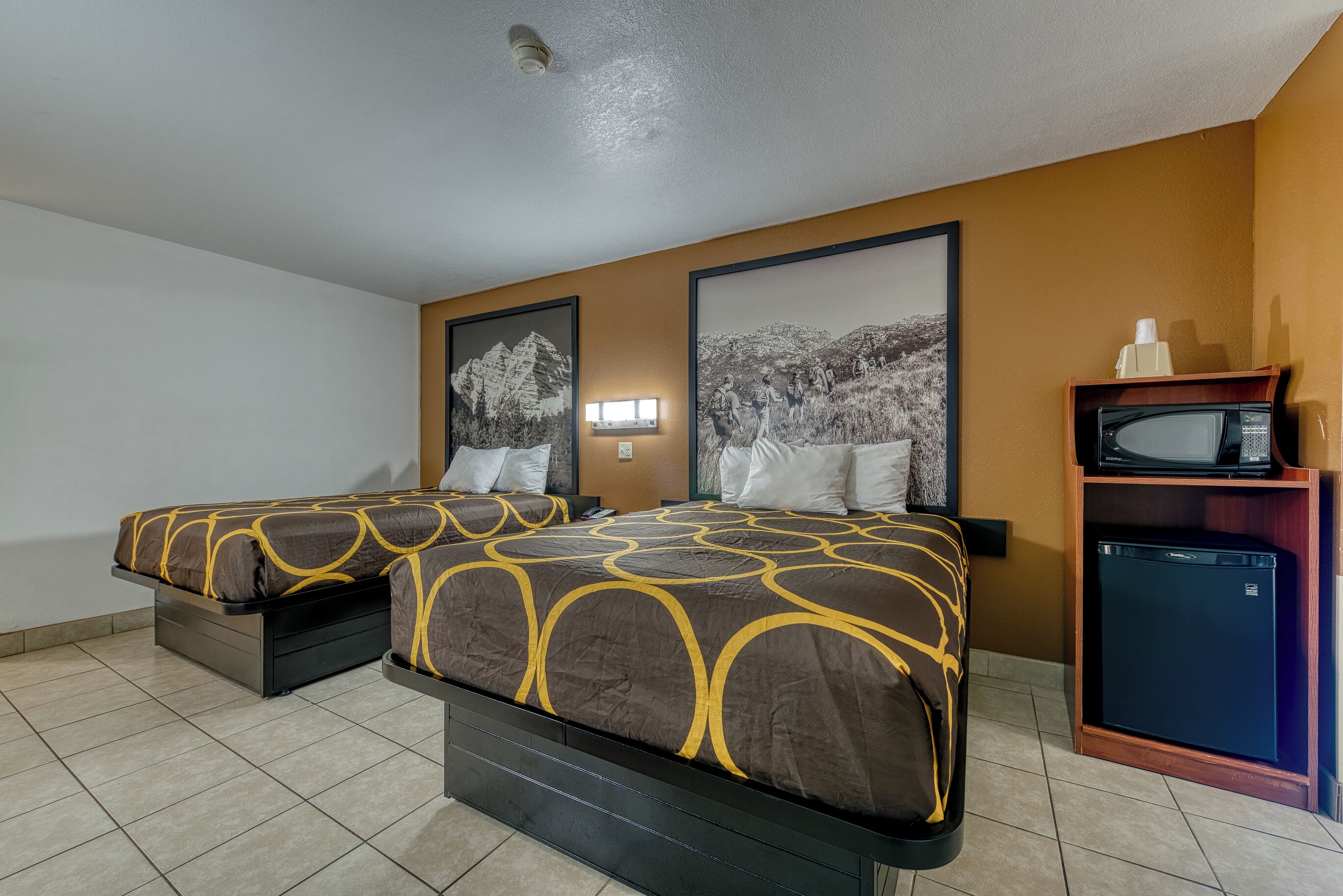 Een hotelkamer met twee bedden, een kleine koelkast en een magnetron op een houten plank.