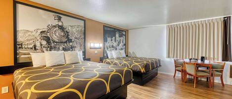 Une chambre d’hôtel avec deux lits, une table à manger avec des chaises et un grand tableau encadré représentant un train, accroché au mur.