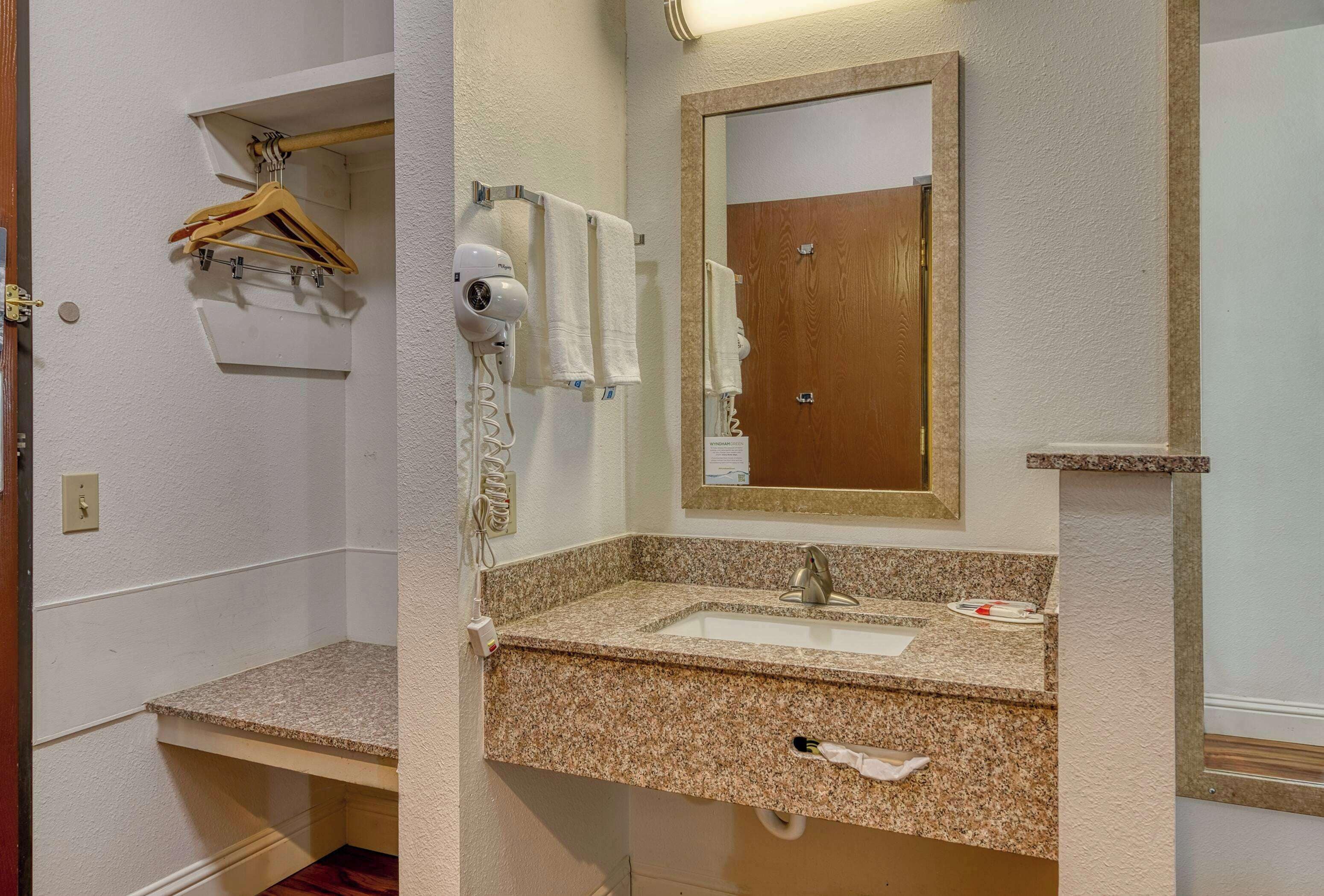 A bathroom with a granite countertop sink, a mirror, a towel rack, and a hairdryer.