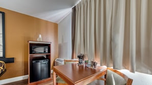 Een compacte hotelkamer met een houten eettafel, een inbouwkoelkast, een magnetron en een kleine kitchenette.