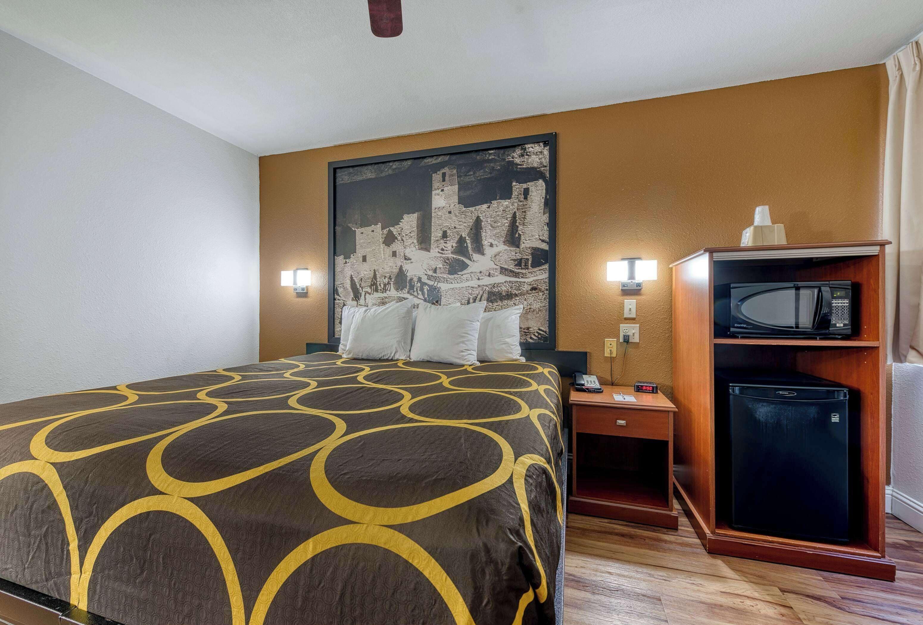 Una habitación de hotel con cama, mesita de noche, microondas y refrigerador.