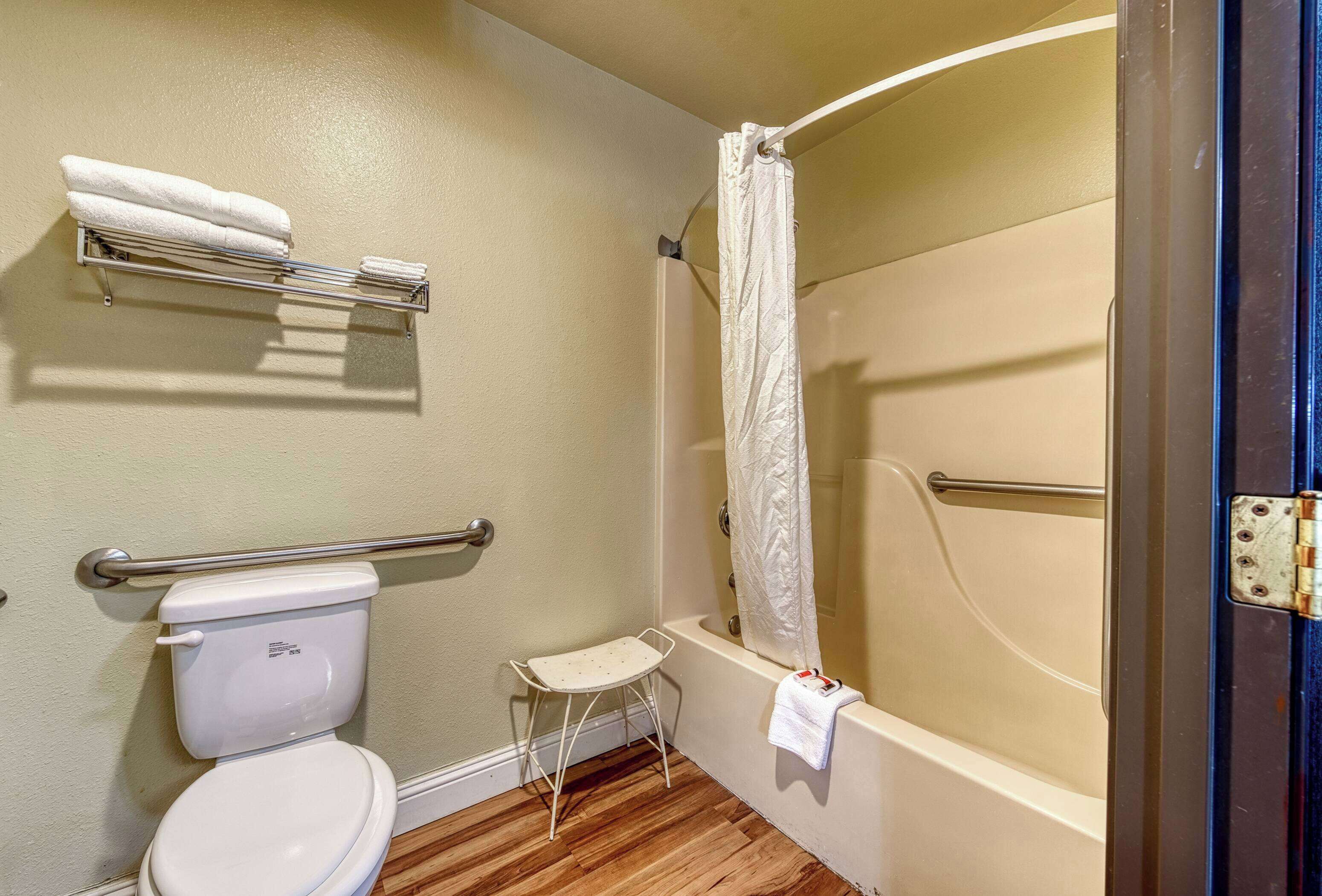 A bathroom with a toilet, a small stool, a towel rack, and a bathtub with a shower curtain.