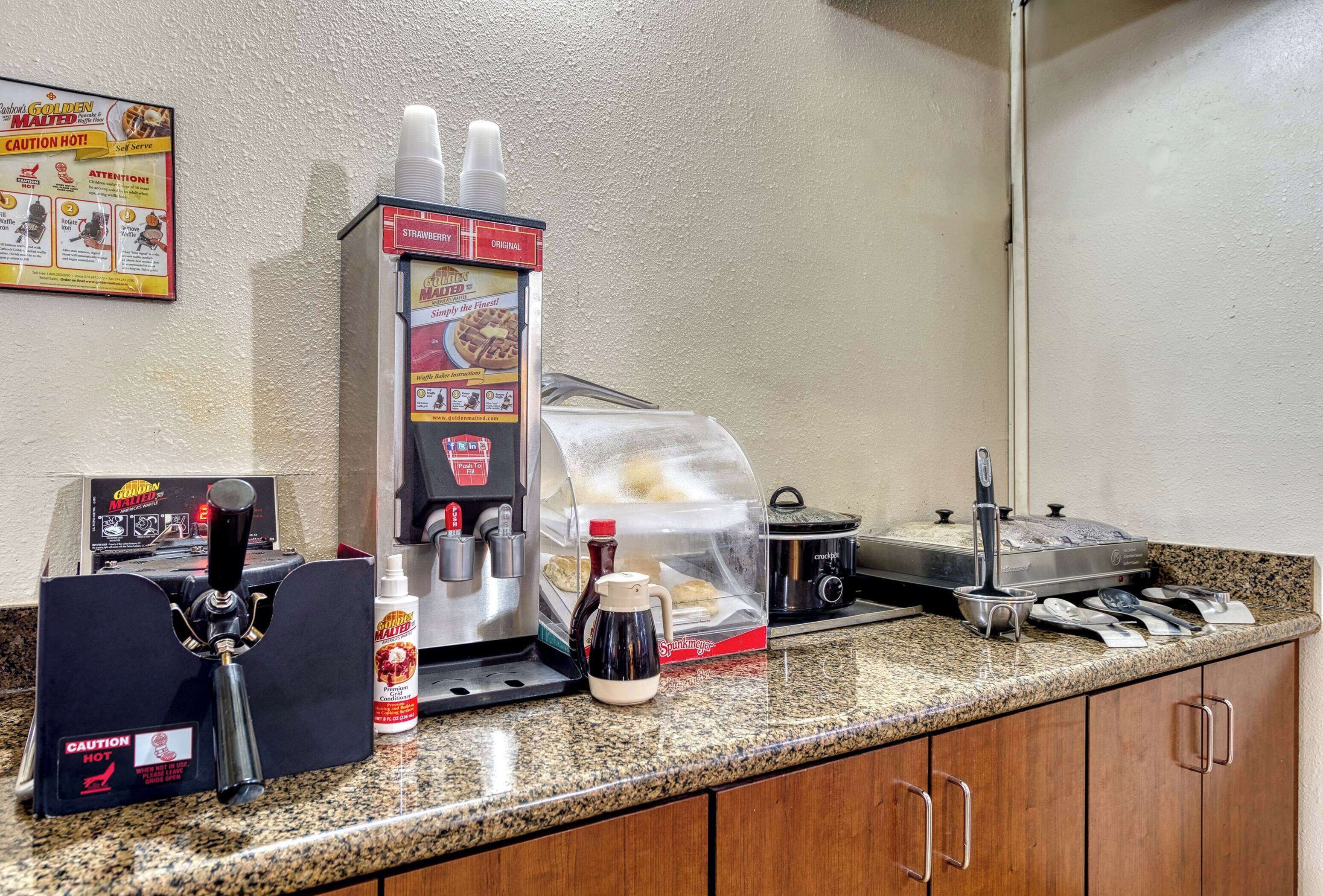 A coffee station with a coffee machine, a milk frother, a coffee pot, and a container of coffee creamer.